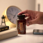 Cápsulas Moles MetaPWR doTERRA — mão a segurar frasco em secretária com relógio dourado, suplemento bem-estar natural