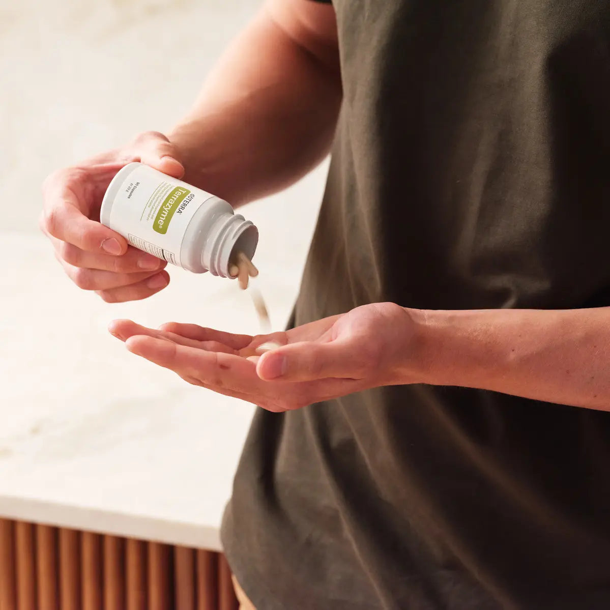 TerraZyme doTERRA 90 ct — mãos a verter cápsula para a palma da mão na cozinha, suplemento enzimas digestivas CPTG