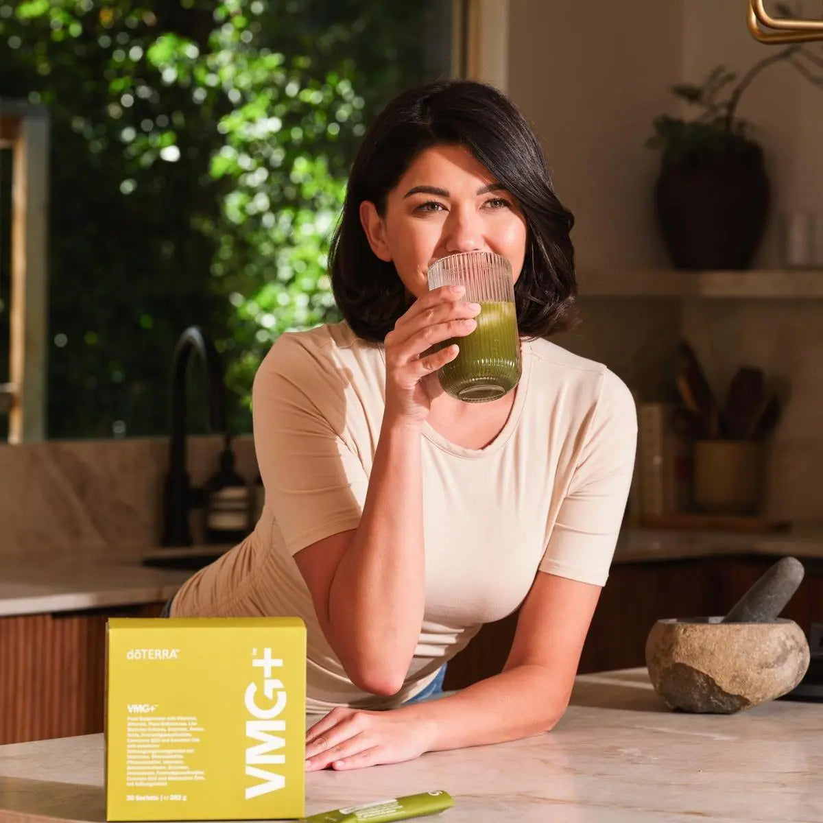 VMG+ doTERRA caixa mulher segurando batido verde na cozinha — suplemento alimentar vegetal puro com nutrientes essenciais CPTG