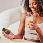 Cápsulas moles Zendocrine doTERRA mulher com cabelo encaracolado segurando frasco preto com vaso no sofá — suplemento detox natural CPTG