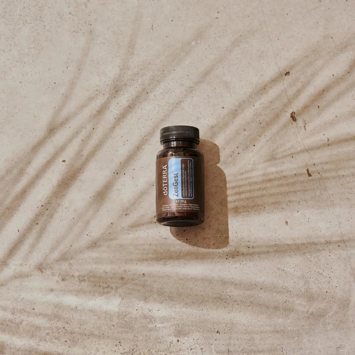Cápsulas moles ZenGest doTERRA frasco na areia com sombras de palmeira vista de cima — suplemento digestivo natural com óleos essenciais CPTG