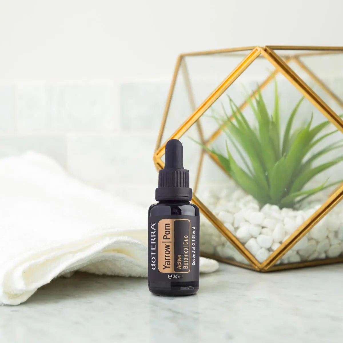 Yarrow Pom doTERRA 30ml em mármore com toalha branca e terrário geométrico dourado — óleo de yarrow e romã natural CPTG