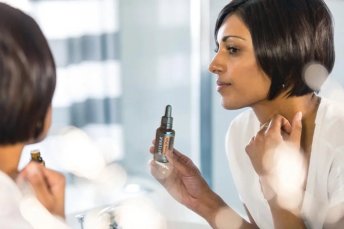 Yarrow Pom doTERRA 30ml mulher ao espelho no banho aplicando no pescoço com conta-gotas — óleo de yarrow e romã puro CPTG